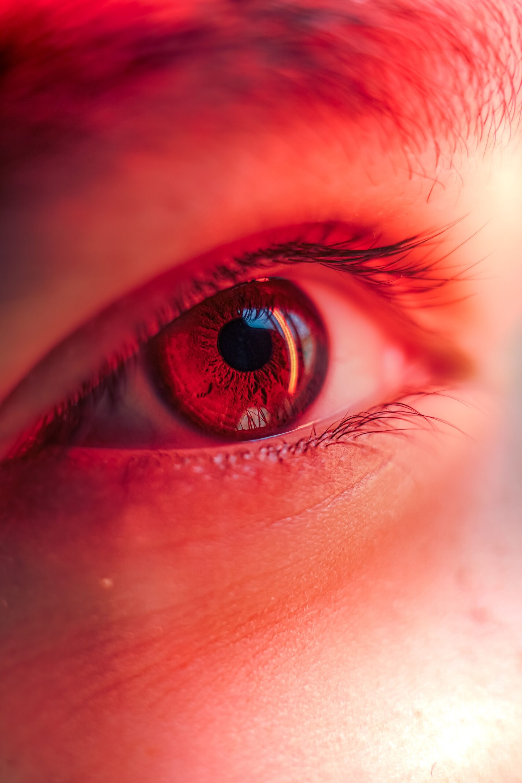 Macro shot of a human eye with a striking red hue, showcasing the pupil and iris.