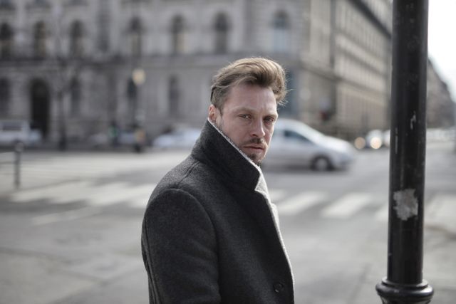 Side view of handsome male wearing classy jacket crossing road on sunny day and looking at camera
